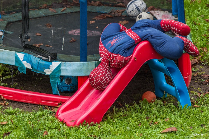 Soft Spiderman doll draped over children's slide in garden by trampoline with footballs. Colour landscape. © P.Maton 2014 eyeteeth.net