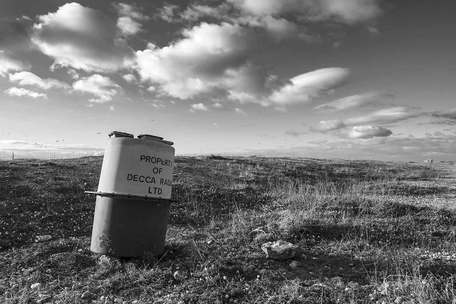 abandoned Decca radar buoy on beach with dead grass and dramatic clouds in sky, Dungeness Kent UK, black and white monochrome landscape portrait © P. Maton 2018 eyeteeth.net